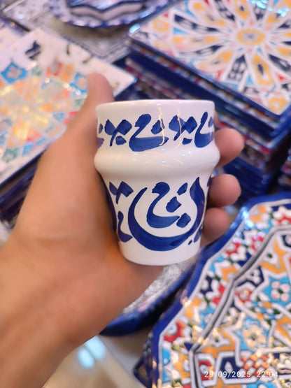 Hand painted dishwasher safe cups featuring Arabic calligraphy, crafted from white clay, displayed in hand.