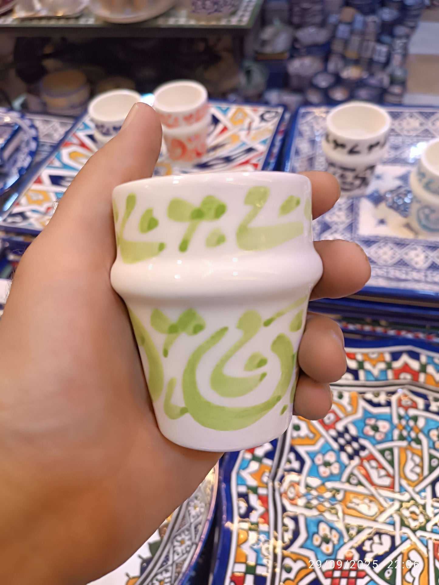 Hand holding a hand painted dishwasher safe cup with green Arabic calligraphy design, showcasing unique craftsmanship.