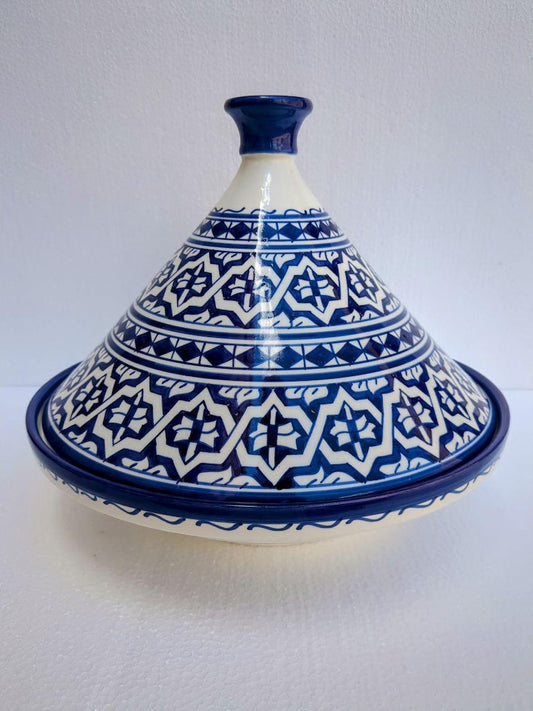 A ceramic tagine pot with a conical lid, decorated with a blue and white geometric pattern, set against a plain light gray background.